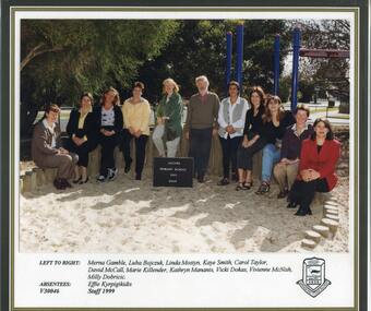 Adults sitting in one row on wooden structure, the school playground visible in background.