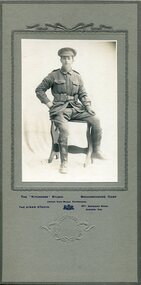 A man in uniform sitting on a chair, with his hand on his hip and the other by his side