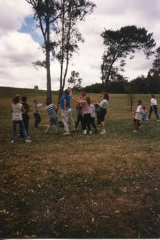 Children and Adults playing a ball game in front of a tree