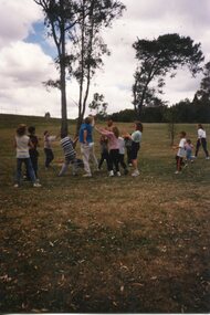 Children and Adults playing a ball game in front of a tree