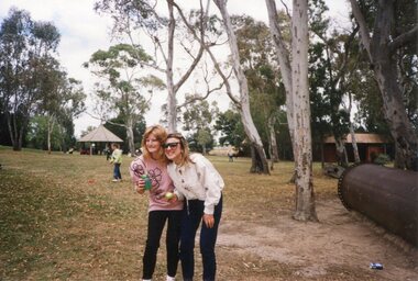 Two adults in a park with children playing behind them.