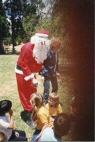 Father Christmas centre, with an adult to his left, and children sitting in front of him. 