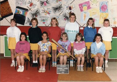 Formal team photograph with children in two rows, those in the front are sitting on chairs. The child in the centre front is holding a softball bat.