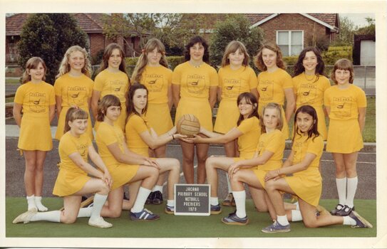 Formal team photograph with children all dressed in yellow in two rows. The front row is kneeling, the two children centre are holding a netball