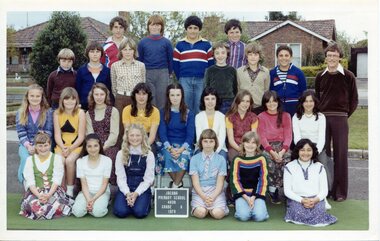 Formal class portrait with children in four rows, the front row
 is kneeling. An adult is standing right of picture next to the third row.