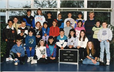 Formal Class portrait with children in three rows, the front row is sitting on the floor. An adult is standing on the right of the photograph in the third row