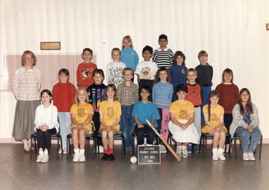 Formal team photograph, with children in four rows the front row is sitting on chairs. An adult is standing on the left in line with the second row