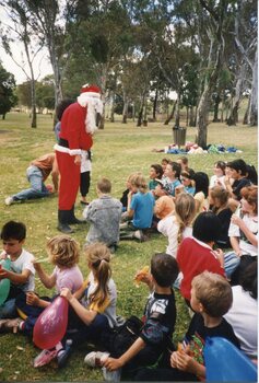 Father Christmas talking to children, sat on the grass in front of him. 