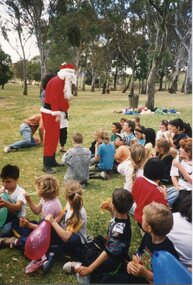 Father Christmas talking to children, sat on the grass in front of him. 