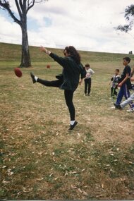 Adult playing football, with children in the park