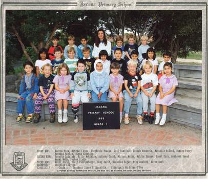 Formal class photograph with children in three rows sitting on wooden benches with an adult in centre of the third row.