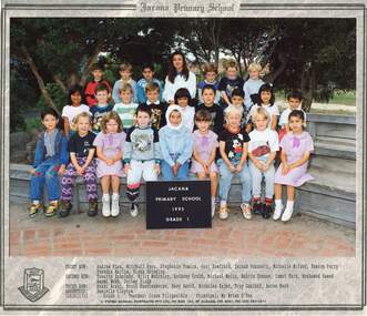 Formal class photograph with children in three rows sitting on wooden benches with an adult in centre of the third row.