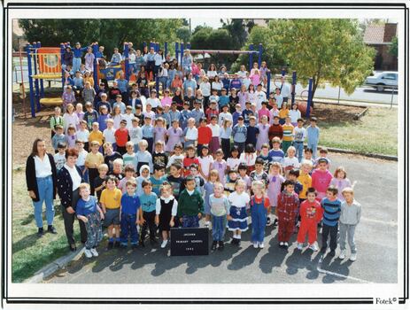 Formal school photograph of children and adults in front of a climbing frame
