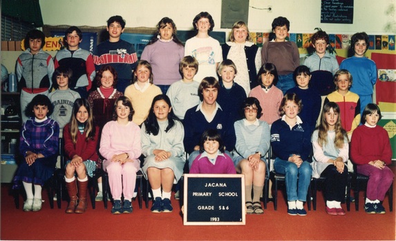 Formal photograph of a child sitting on the floor and other children in three rows with an adult sitting in the centre of the front row. 