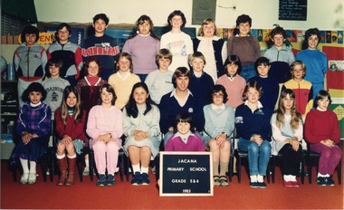 Formal photograph of a child sitting on the floor and other children in three rows with an adult sitting in the centre of the front row. 