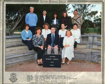 Formal photograph of adults in three rows in front of trees. The two front rows are seated on wooden benches. 