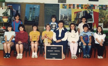 Formal team photograph of children in two rows, back row standing, with an adult right of centre in the front row