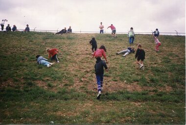 Children climbing and rolling down a slope, climbing back up and sitting at top