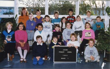 Children in four rows for a class photograph with an adult on the left in the back row