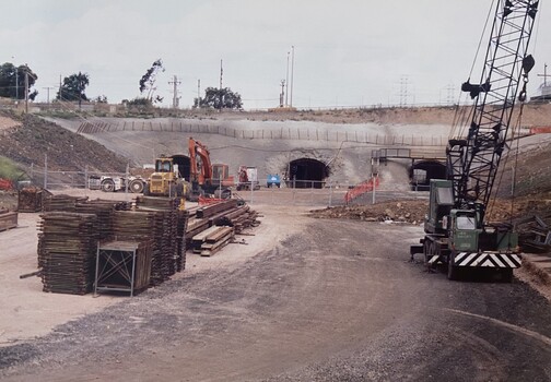A Construction site with various large machinery and tunnels in the background.