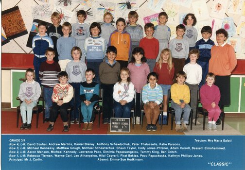 A formal school photograph with children in four rows, those in the front row are seated, on the right of the second row, is an adult standing.