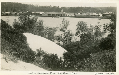 Postcard - the Central Hotel, butcher shop, bluestone wall at lake edge, and two small jetties. Sand hills and natural vegetation in foreground. Lakes Entrance Victoria, 1930c
