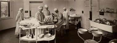 Operation in progress, Children's Hospital, Carlton, circa 1920. Long shot of interior of hospital room. Bed is positioned in the middle with patient lying on the bed, staff are positioned around the bed. The room consists of medical equipment and technology of that era.
