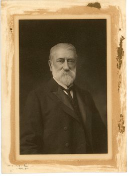 Portrait of an older man wearing a dark suit.  He has silver grey hair a beard and moustache.  He is facing the camera.