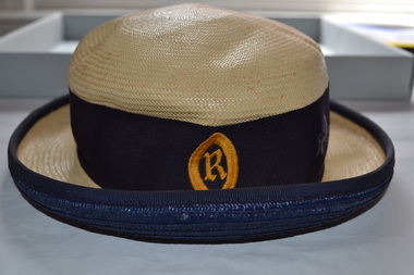 Cream coloured straw hat with blue ribbon band.  The band features a yellow gold school crest.