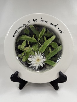 Front of ceramic plate with flower print and an inscription "Happiness is here & now"