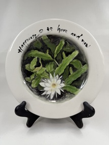 Front of ceramic plate with flower print and an inscription "Happiness is here & now"