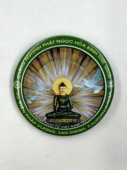 Front of a badge featuring the seated Jade Buddha surrounded by rays of light, with doves soaring above, commemorating its exhibition in San Diego, 2010.