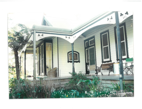 The exterior of an old cream coloured house. The verandah is prominent in the background and plants in the foreground. 