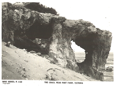 Rocky outcrop with two large holes through, sandy dune and sea in background