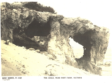 Rocky outcrop with large holes through, sandy bank and sea in back ground