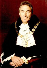 Coloured portrait photograph of Reg Harry in Mayoral Robes with gold mayoral chain around neck and whit frilled jabot at neck 