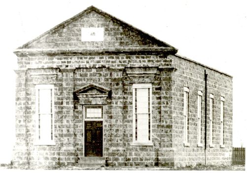 Large bluestone church with tall narrow windows either side of double door entrance with two steps 