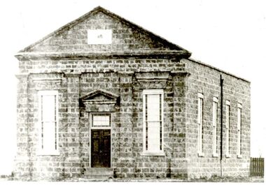 Large bluestone church with tall narrow windows either side of double door entrance with two steps 