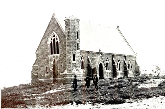 Large bluestone church with tower with crosses on gable ends and 3 panel arched windows