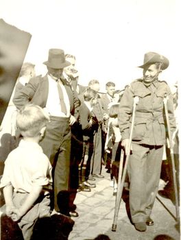 Group of men and boys surrounding a soldier in uniform on crutches