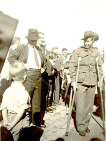 Group of men and boys surrounding a soldier in uniform on crutches