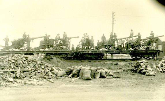 Soldiers standing on train carriages with guns and gun carriages aboard