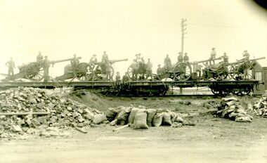 Soldiers standing on train carriages with guns and gun carriages aboard