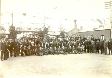 Large group of people posed with road archway in background Welcome Home 1921