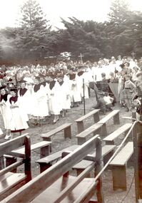 St John’s choir in white robes with wide collars and mortar board style hats, wooden benches in forground