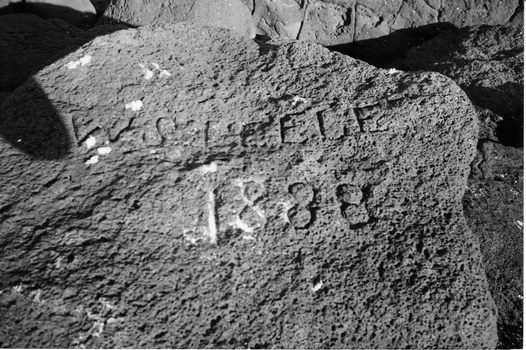 Black and white photograph of large bluestone boulder with the name W Steele 1888 Carved into the surface