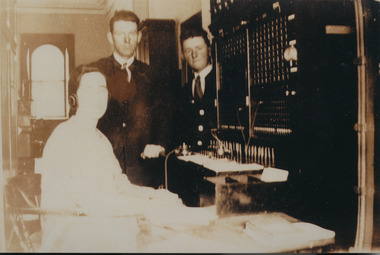 Two men and a woman telephonist  gathered around the telephone exchange desk