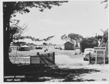 Wooden pailing entrance to camping ground with caravans and cars. A toilet block can be seen on the right.