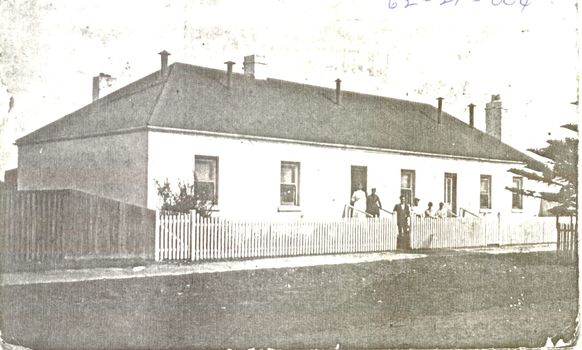 Large house with two front doors with males and females posed in front 