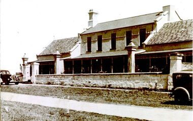 Exterior of hospital with verandah stone fence and gates two cars 